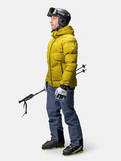 Ein Mann in einer Halti Nordic Arcty II Skijacke Herren hält Skistöcke vor einem weißen Hintergrund.