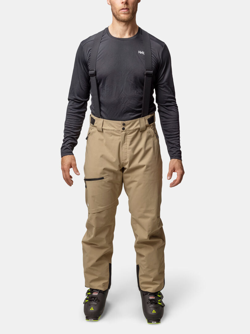 Eine Person in Halti Carvey II DX Skihose Herren mit DrymaxX tech, schwarzen Hosenträgern, dunklem Hemd und schwarzen Skischuhen.
