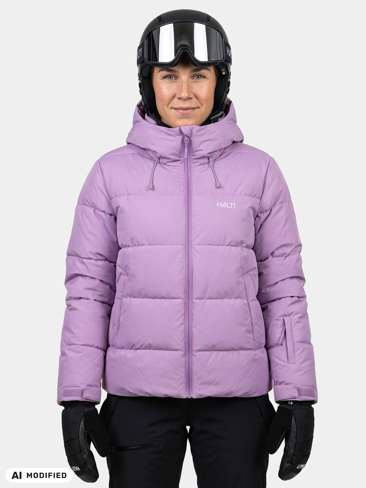 Eine Person, die eine lavendelfarbene Halti Ascloud Puffer Skijacke für Damen, einen Skihelm und schwarze Handschuhe trägt.