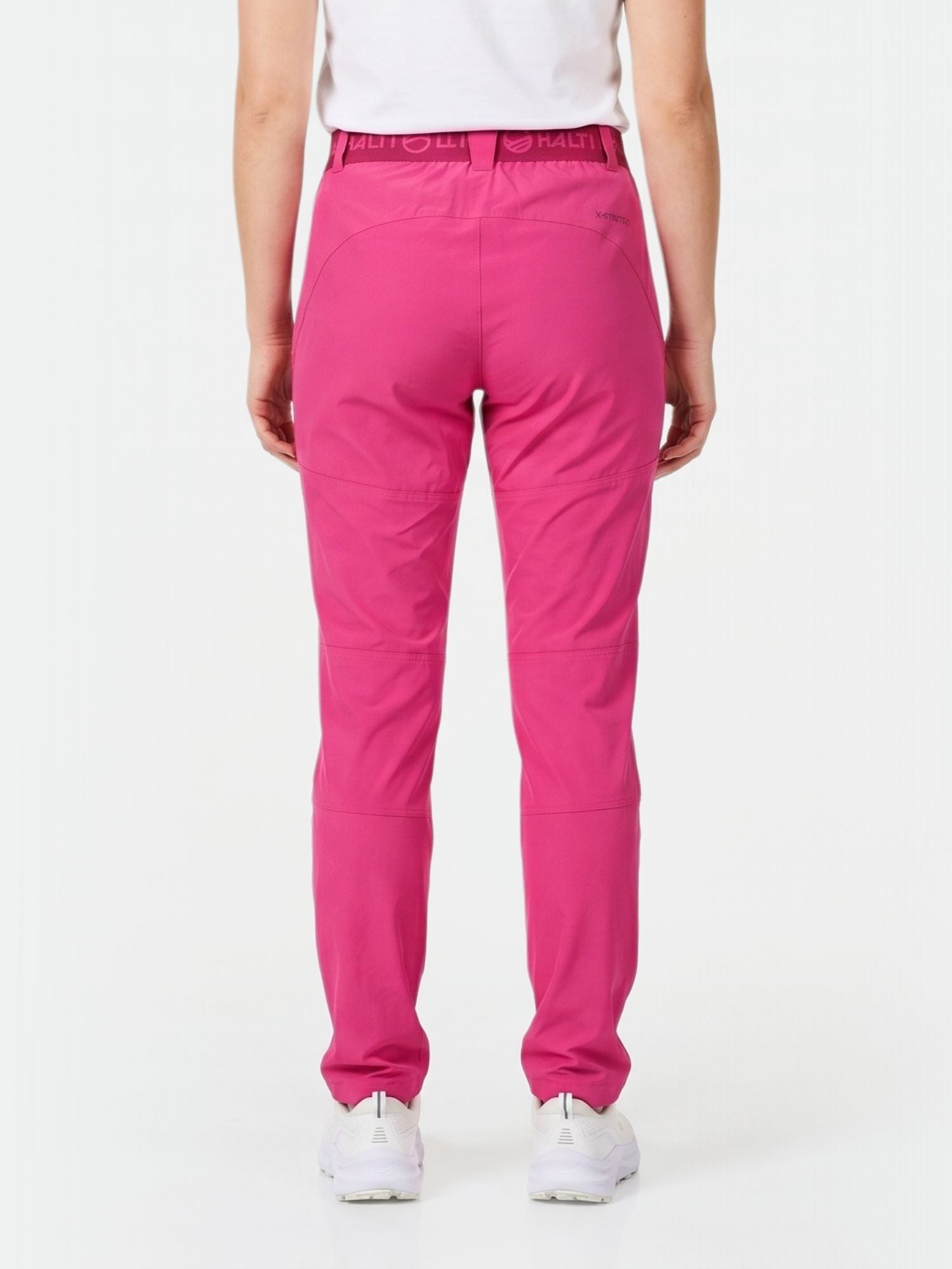 Person in hellrosa Halti Pallas Damen X-stretch Lite Hose und weißen Turnschuhen, von hinten gesehen auf weiß.
