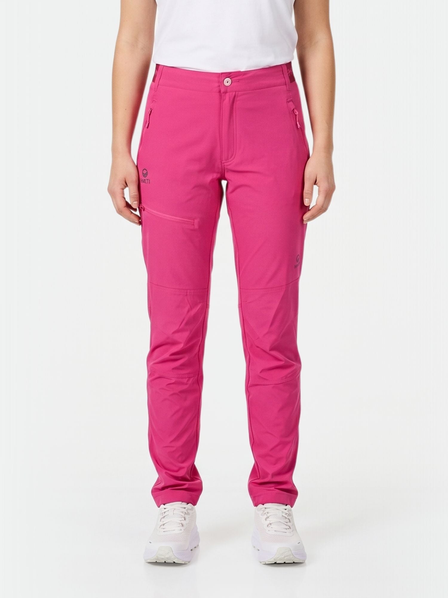 Eine Person in rosa Halti Pallas Damen X-stretch Lite Hose, weißem T-Shirt und Turnschuhen steht mit dem Gesicht nach vorne vor einem schlichten Hintergrund.