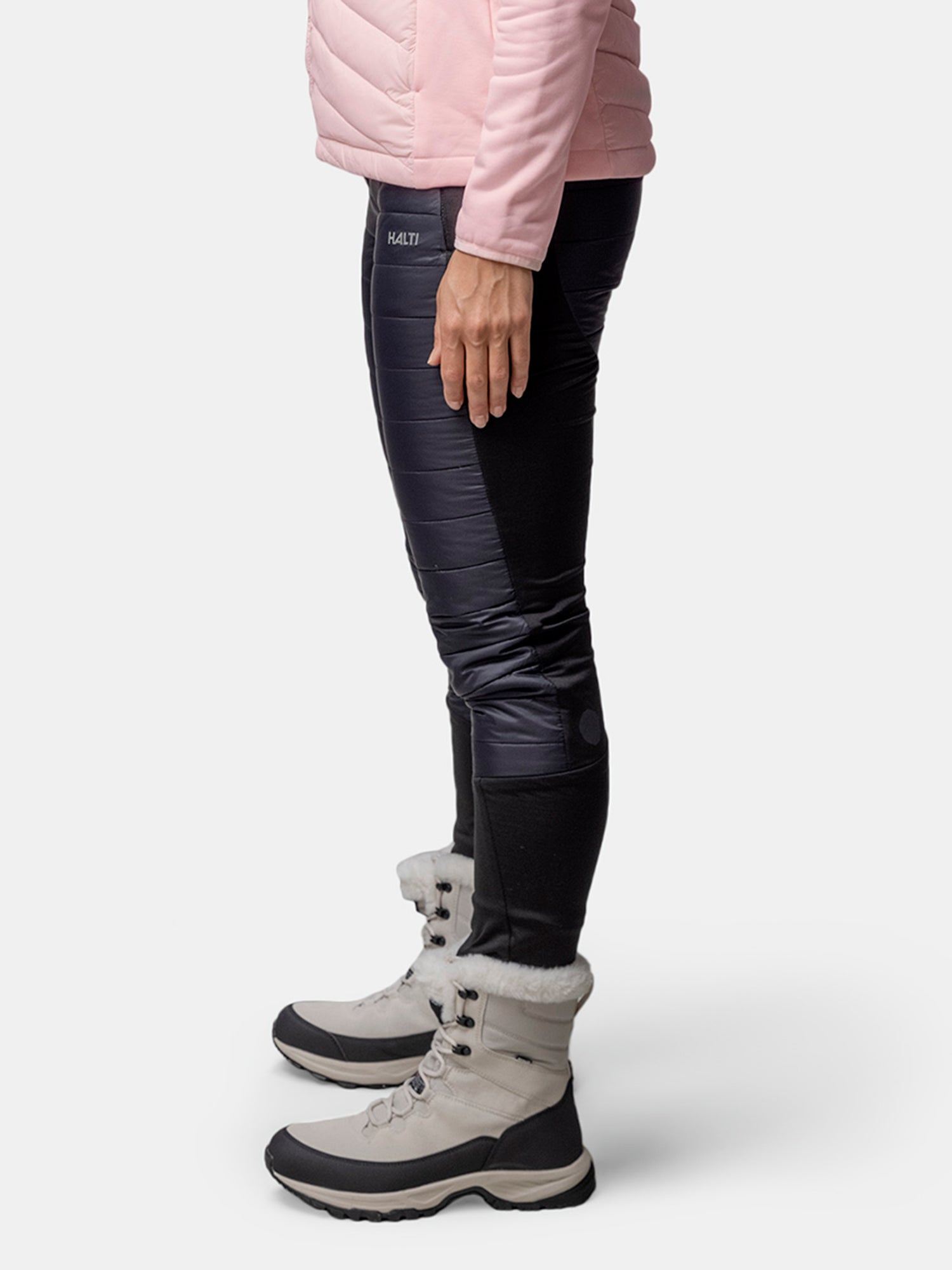 Eine Person in rosa Jacke, Halti Veidnes Isolierhose Damen und hellgrauen Winterstiefeln steht auf weißem Hintergrund.