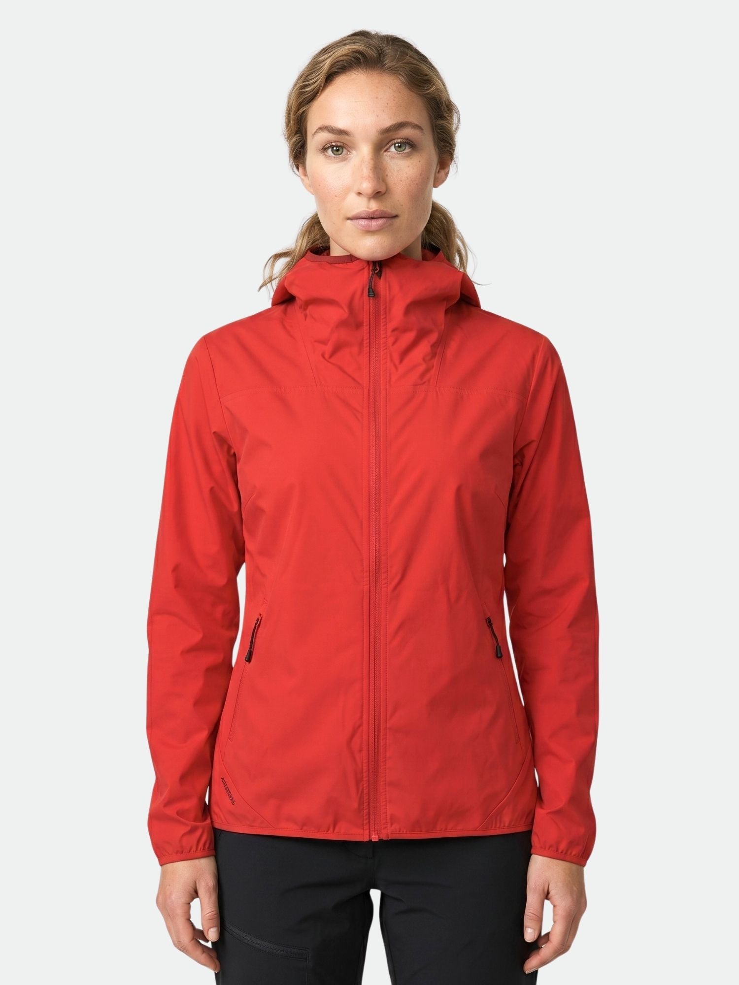 Eine Frau in einer roten Halti Pallas Damen Lite X-stretch Jacke und einer schwarzen Hose steht vor einem schlichten hellen Hintergrund.