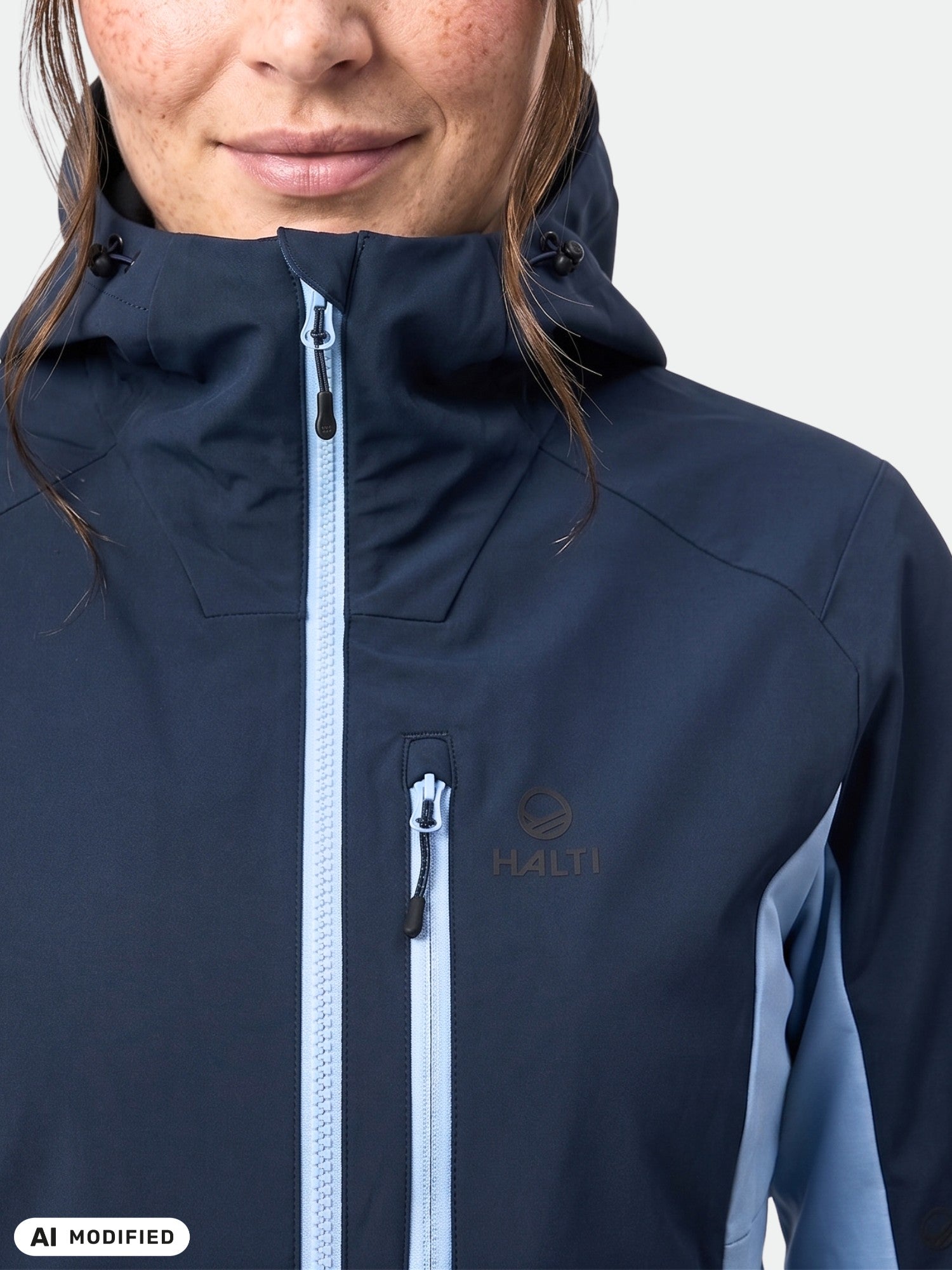 Person in einer marineblauen „Pallas Plus III Damen Warm Hybrid Jacke“ von Halti, hellblaue Reißverschlüsse, einfarbiger Hintergrund.