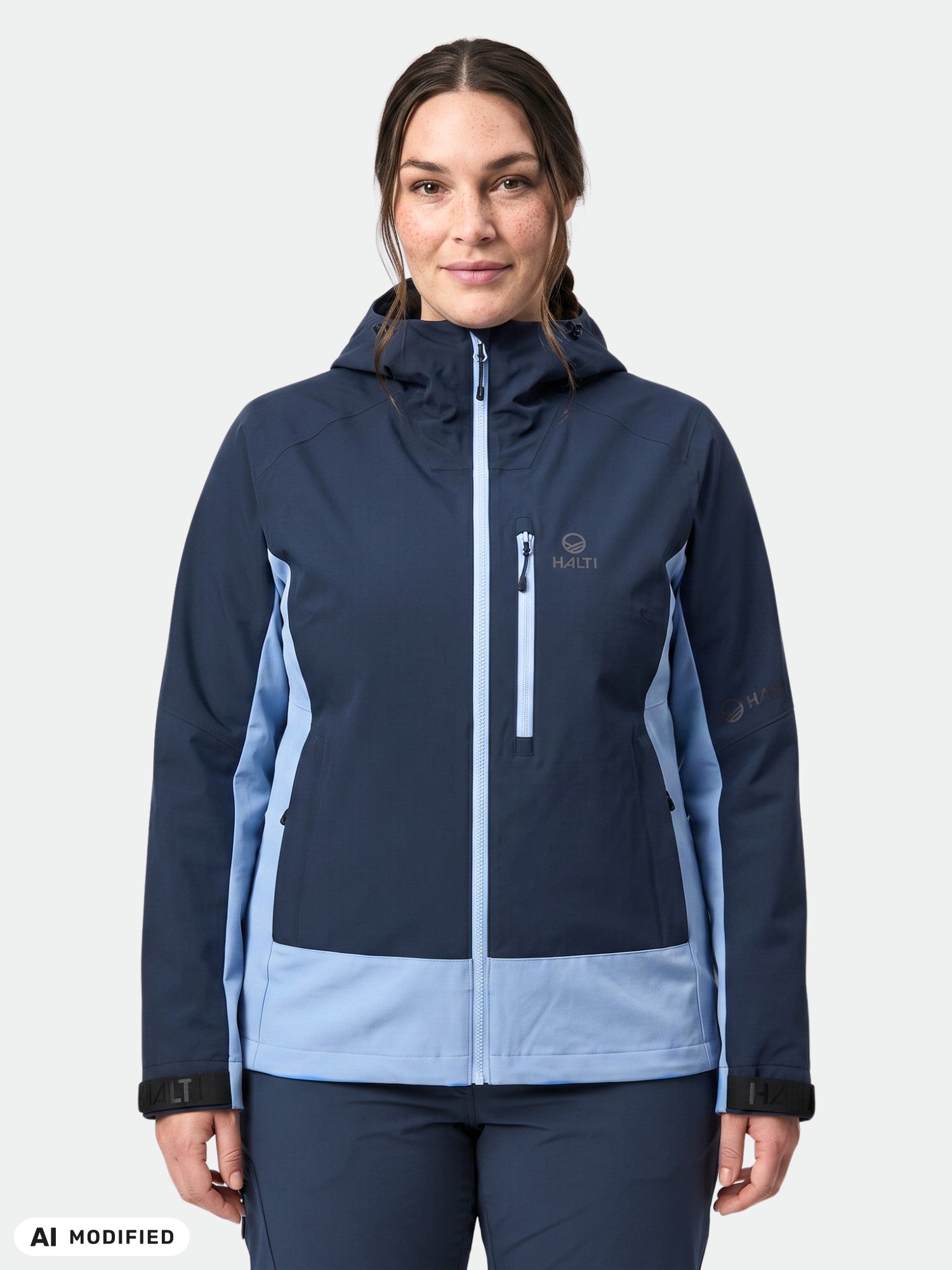 Eine Frau trägt die Halti Pallas Plus III Damen Warm Hybrid Jacke und blickt vor sich hin vor einem weißen Hintergrund.