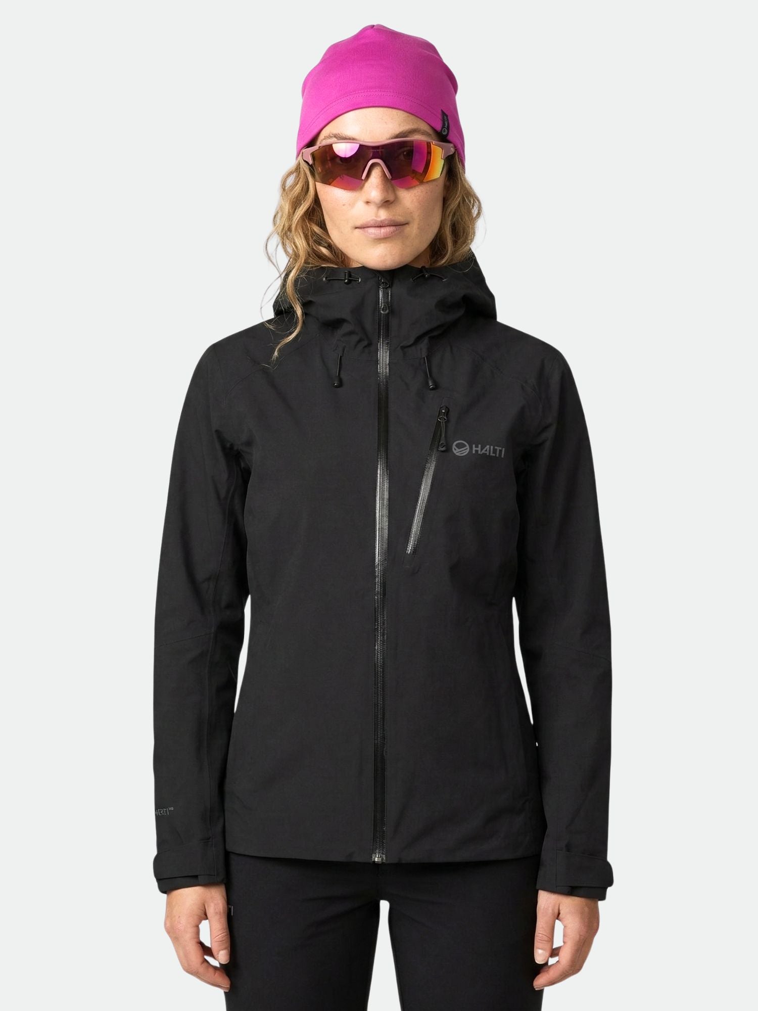 Eine Person in schwarzer Halti Biegga DX Regenjacke Damen, rosa Mütze und reflektierender Sonnenbrille steht mit dem Gesicht nach vorne.