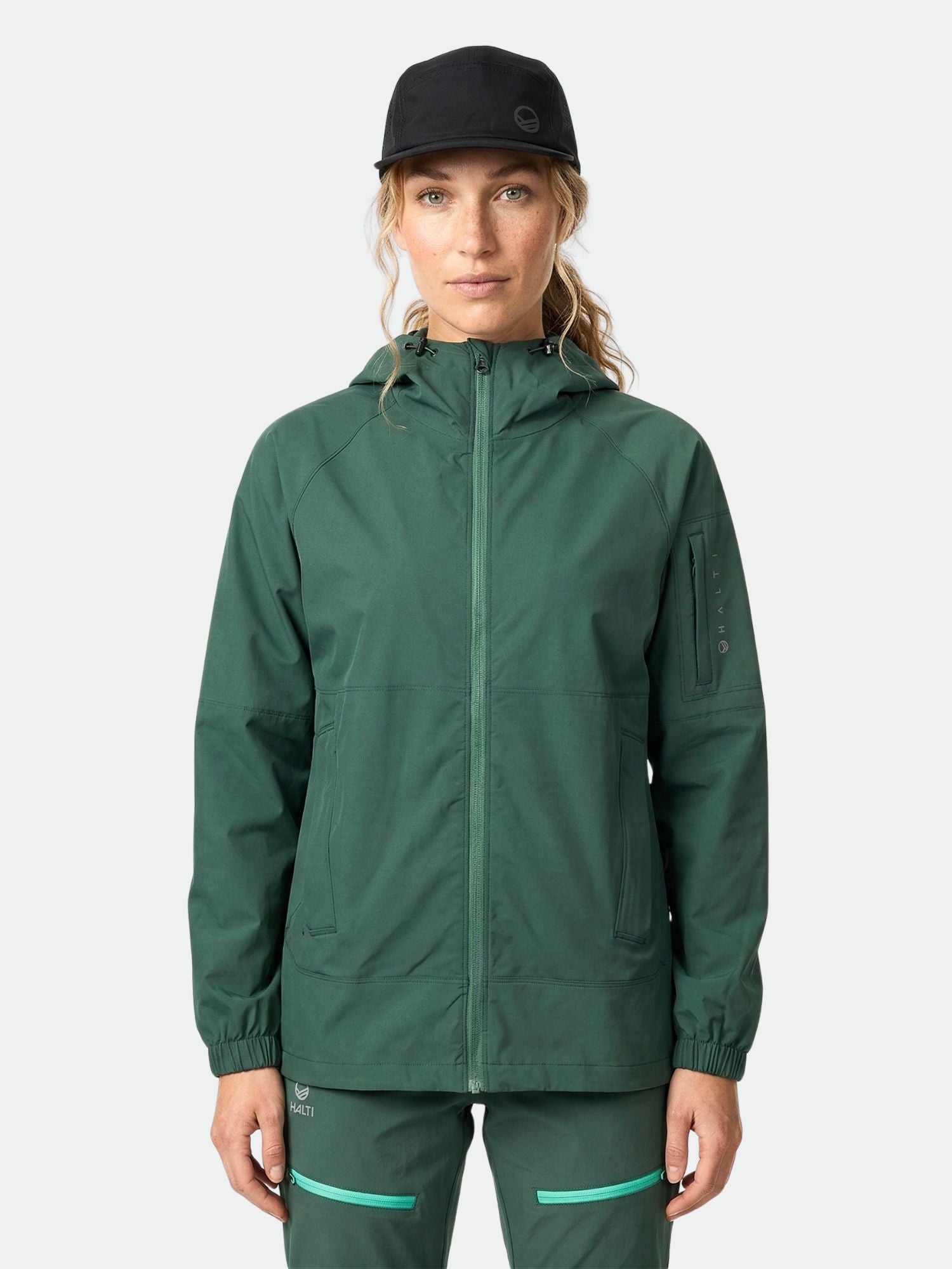 Eine Frau in einer Halti Pallas Damen Jogger Lite Jacke und einer schwarzen Mütze steht mit dem Gesicht nach vorne vor einem schlichten Hintergrund.