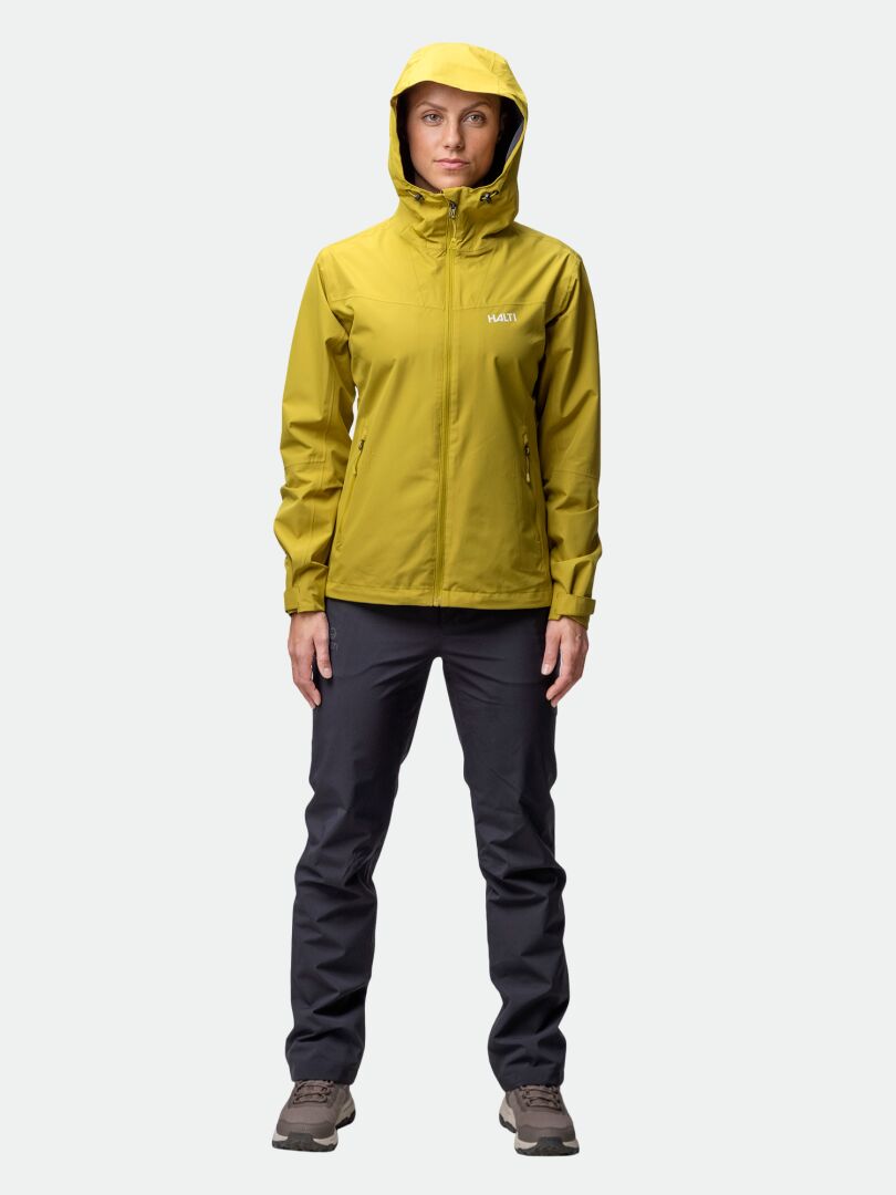 Eine Person steht mit dem Gesicht nach vorne in einer gelben Halti Forter DX Regenjacke Damen, perfekt für Aktivitäten im Freien.