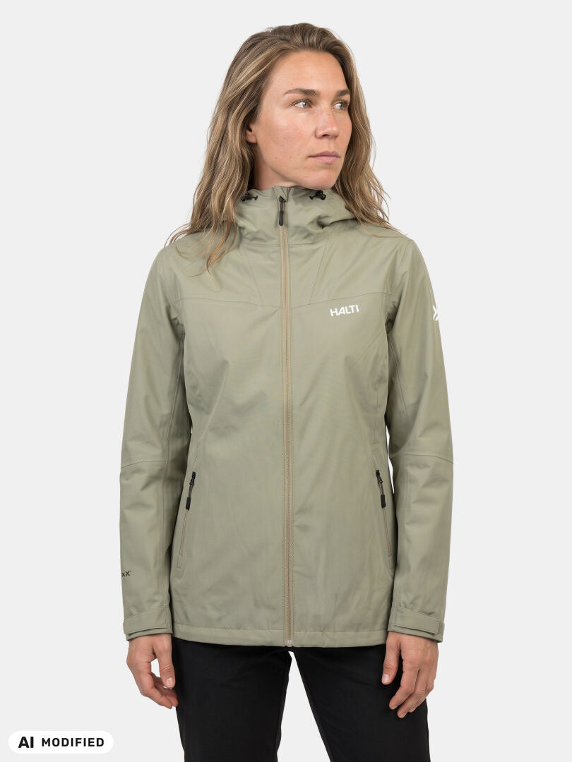 Frau in einer hellgrünen Halti Forter DX Regenjacke für Damen mit Reißverschlusstaschen, die vor einem weißen Hintergrund steht.