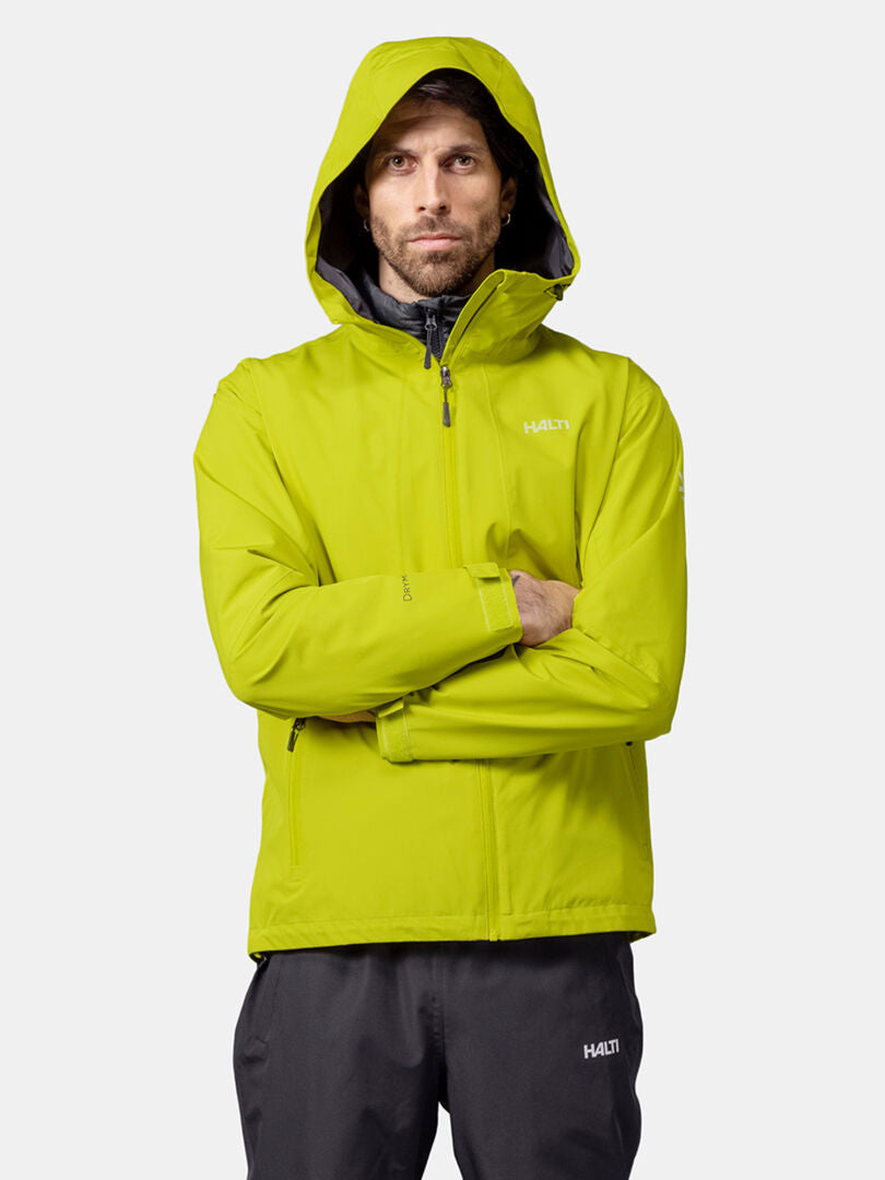 Ein Mann in einer leuchtend gelben Halti Forter DX Regenjacke Herren und einer schwarzen Hose steht mit verschränkten Armen vor einem schlichten Hintergrund.