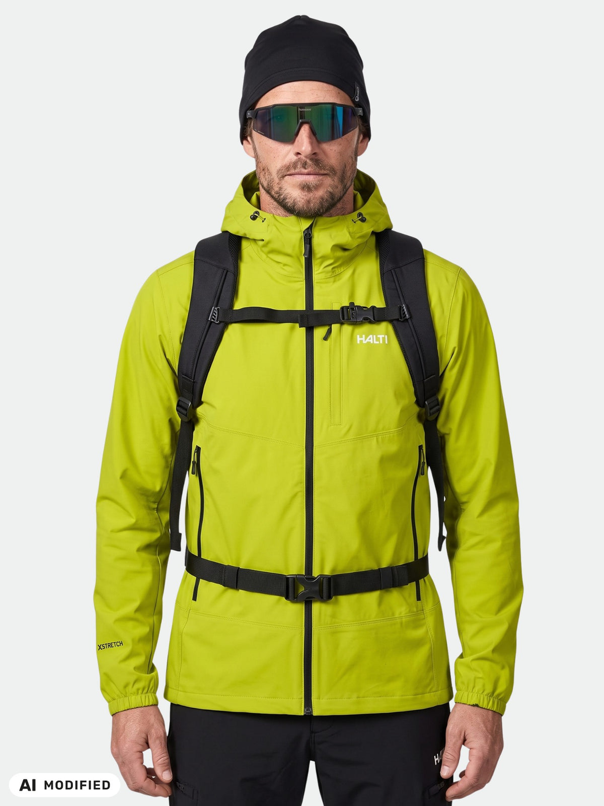 Mann in einer limettengrünen Halti Pallas Evo X-Stretch-Jacke für Herren, mit schwarzer Mütze, Sonnenbrille und Rucksack vor weißem Hintergrund.