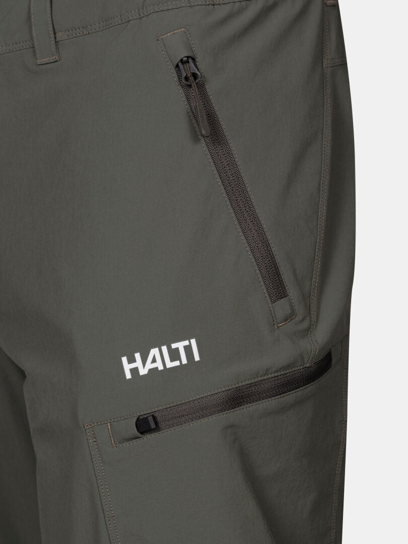 Nahaufnahme der grünen Halti Pallas Evo X-Stretch Herrenhose mit zwei Reißverschlusstaschen und weißem Logo über dem Knie.