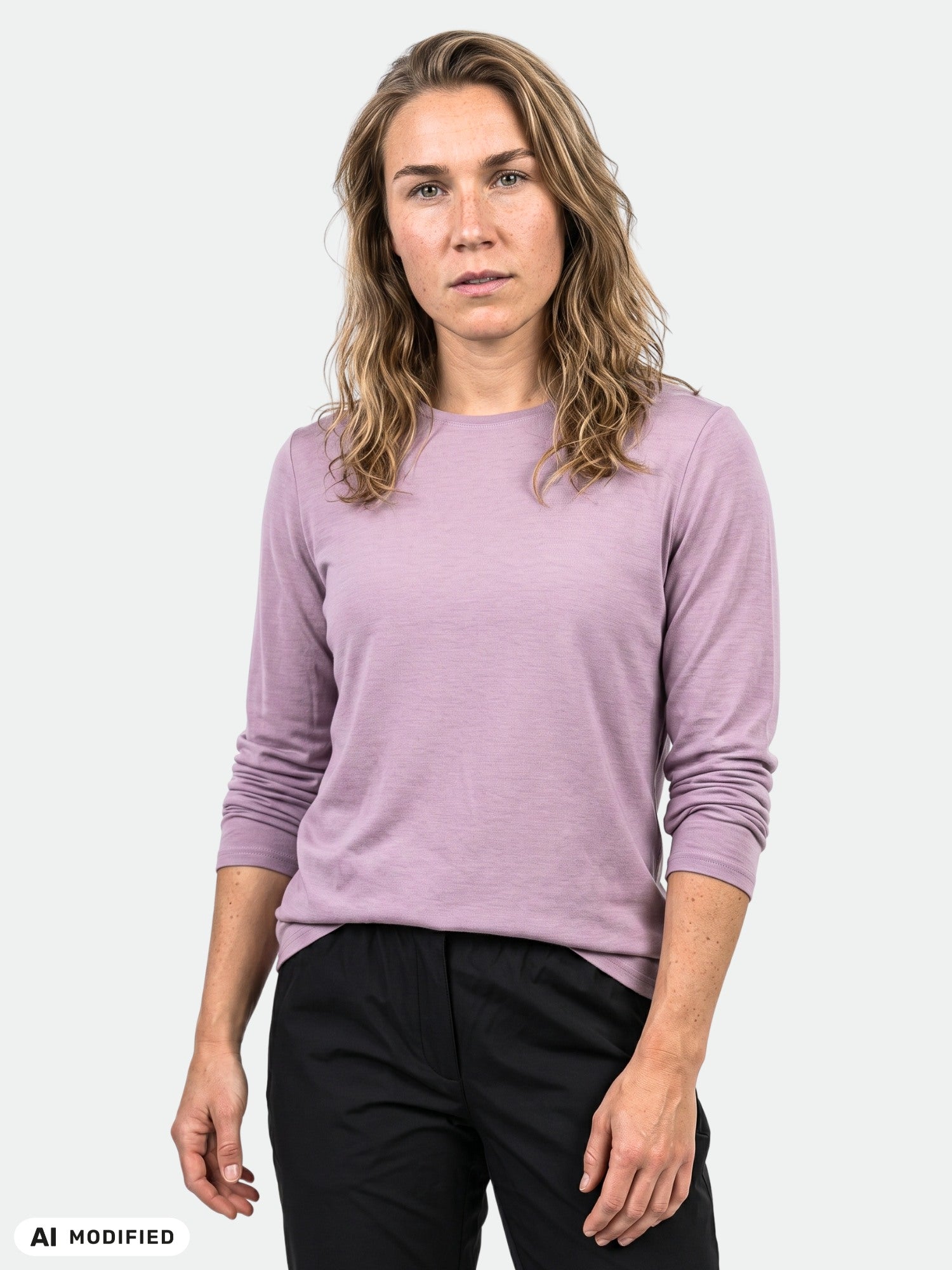 Eine Person mit welligem, hellbraunem Haar trägt ein „Halti Tuntu II Longsleeve Merinoshirt Damen“ in Mauve und eine schwarze Hose.