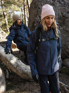 Zwei Personen in Jacken, Handschuhen und Halti Pehmee Merino Mütze wandern durch einen Wald mit Felsen und umgestürzten Bäumen.