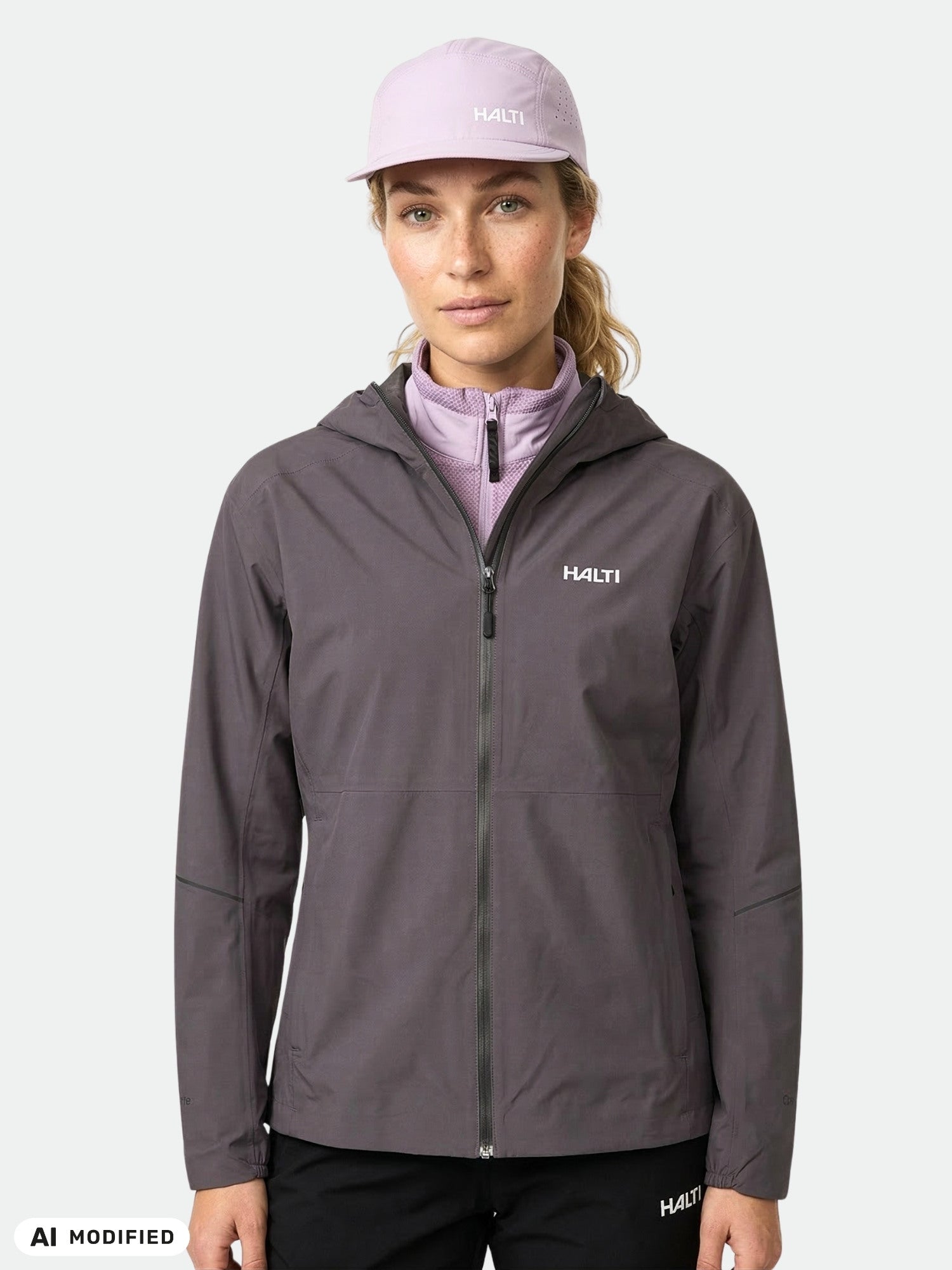Eine Frau trägt eine Halti Pisarat 2,5L DX Regenjacke für Damen, eine hellviolette Mütze und eine schwarze Hose zum Schutz vor dem Wetter.