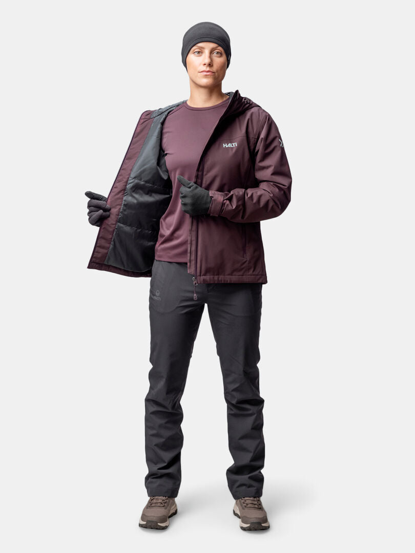 Person, die eine kastanienbraune Halti Forter DX Warm Regenjacke Damen, eine schwarze Hose und Handschuhe vor einem weißen Hintergrund trägt.