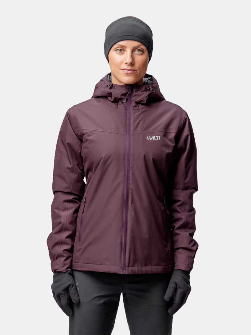 Eine Frau in einer kastanienbraunen Halti Forter DX Warm Regenjacke steht mit dem Gesicht nach vorne vor einem schlichten Hintergrund.