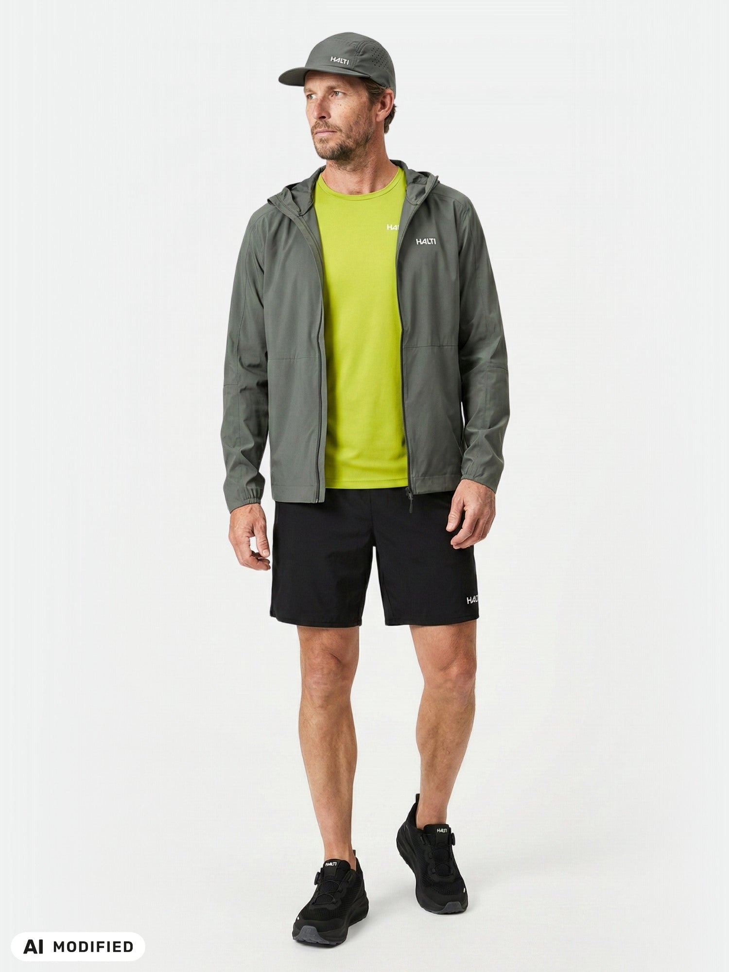 Mann in einer „Halti Pisarat 2,5L DX“-Regenjacke, einem limettengrünen Hemd, schwarzen Shorts und Sneakers sowie einer grauen Mütze.