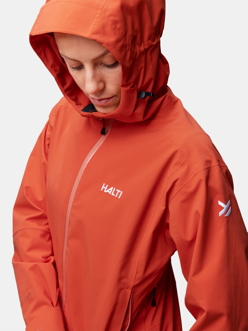 Person trägt eine orangefarbene Halti Staala DrymaxX Regenjacke Damen mit Logos auf Brust und Ärmel.