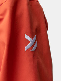 Nahaufnahme des orangefarbenen Halti Staala DrymaxX Regenjacke Damen-Stoffes mit weißem gesticktem geometrischem Logo.