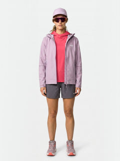 Eine Frau mit rosafarbener Kappe, Sonnenbrille, Halti Staala DX Regenjacke Damen, rotem Hemd, grauen Shorts und rosa-grauen Turnschuhen steht mit dem Gesicht nach vorne.