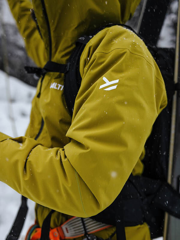 Eine Person trägt die Halti Staala DX Regenjacke Herren mit Logo am Ärmel und Ausrüstung für ein Schneeabenteuer.