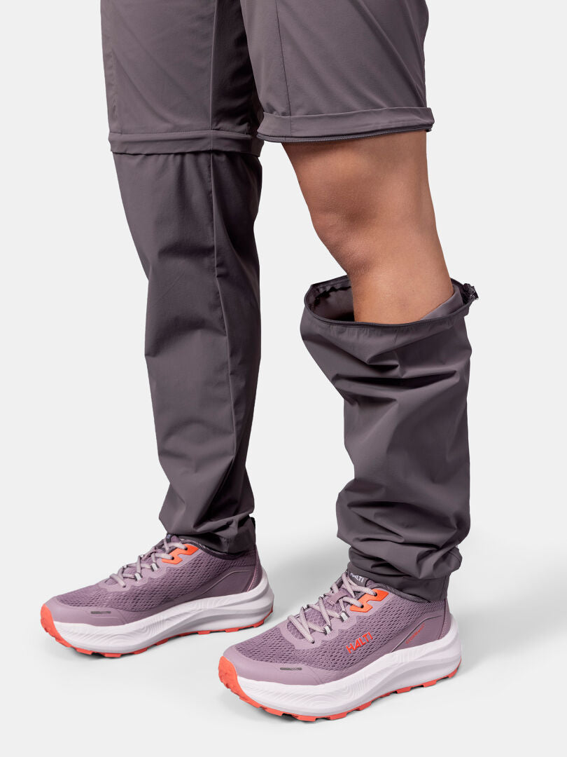 Person trägt Halti Pallas Cool Stretch Zip-off Hosen Damen mit freiliegenden Knien und lila Laufschuhen mit orangefarbenen Akzenten.