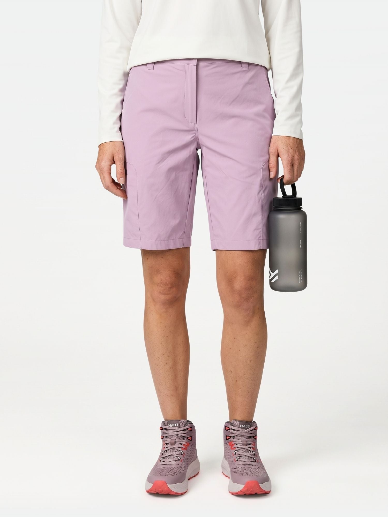 Person trägt Halti Pallas Cool Shorts Damen, weißes langärmeliges Hemd, rosa Turnschuhe, hält eine Wasserflasche in der rechten Hand.