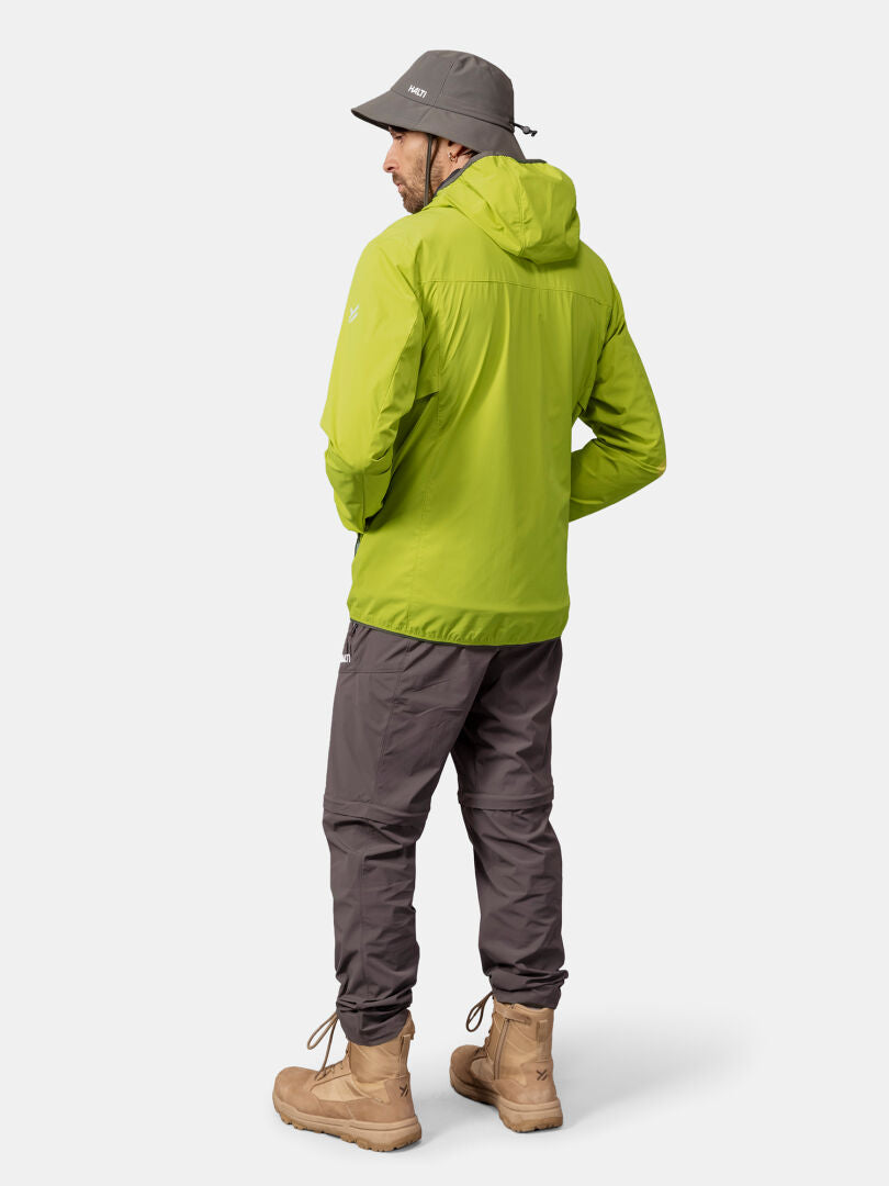 Ein Mann in einer grünen Halti Pallas Cool X-stretch Herren Jacke mit UPF 50+, grauer Hose und hellbraunen Stiefeln, mit dem Rücken zur Kamera.