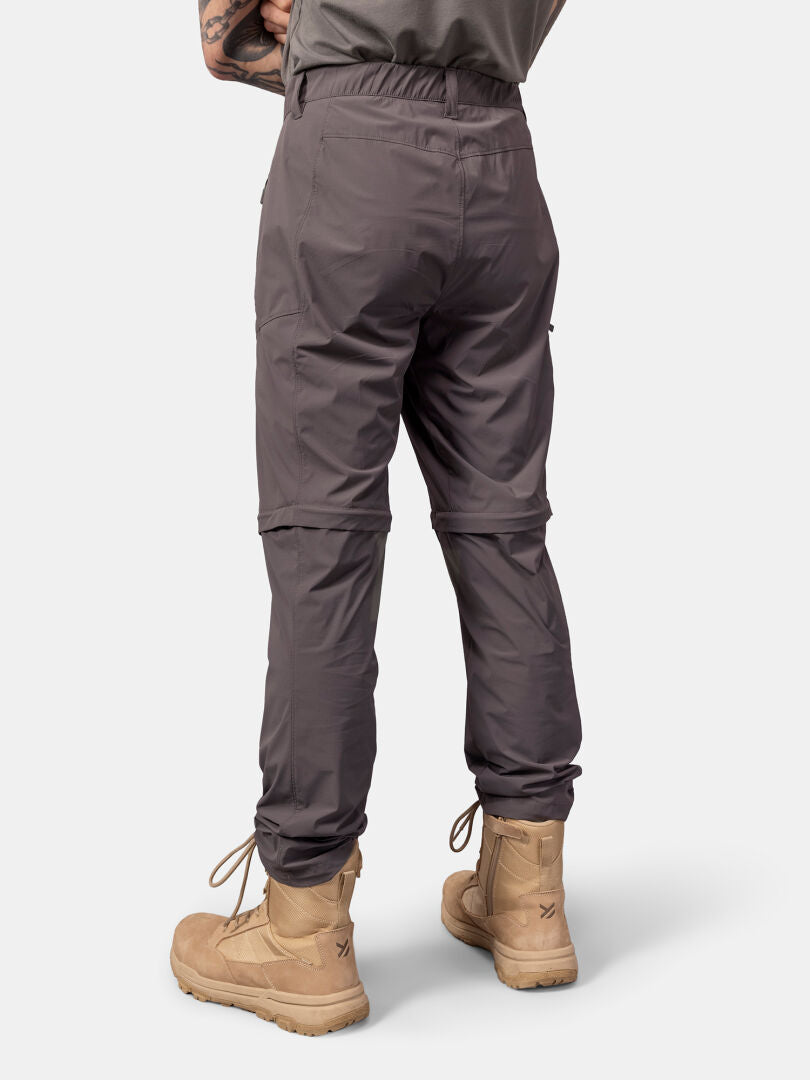 Eine Person trägt Halti Pallas Cool Stretch Zip-off Hosen Herren und hellbraune Stiefel, dargestellt von hinten auf einem schlichten hellen Hintergrund.