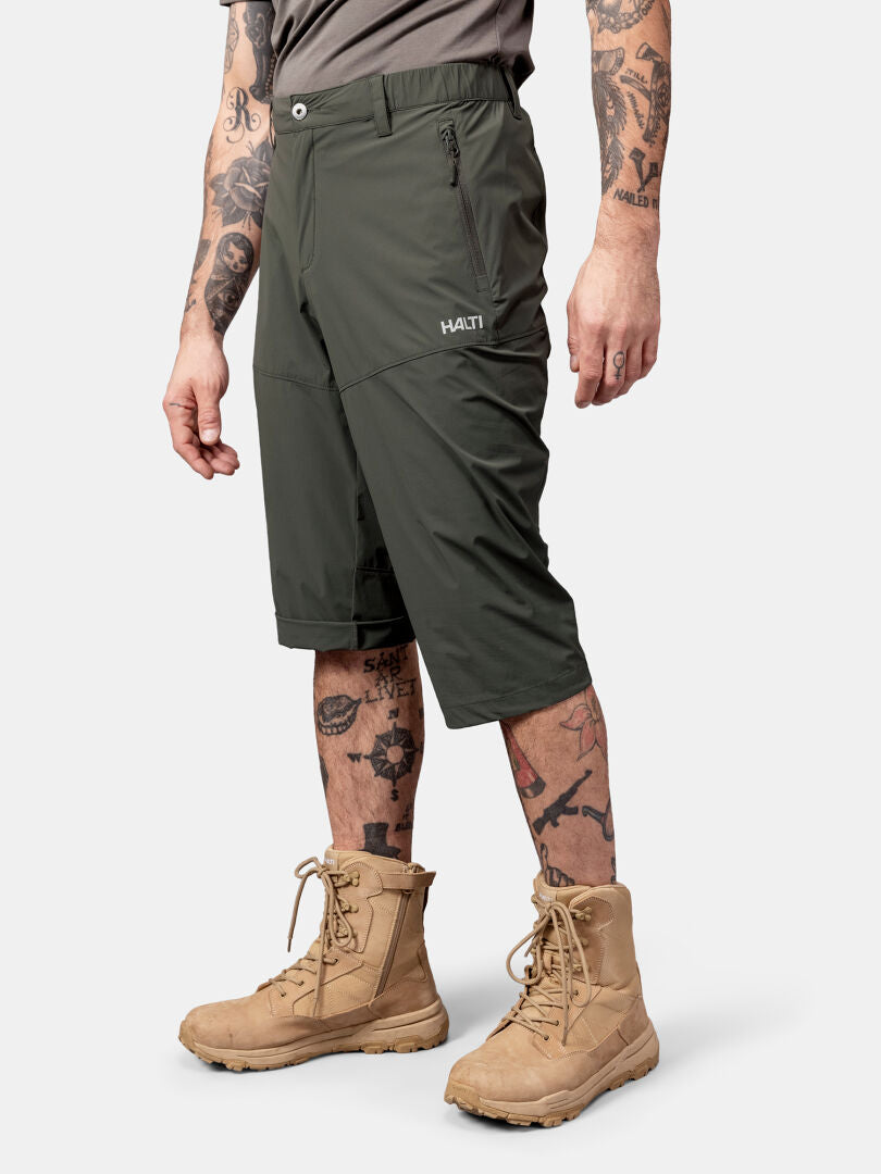 Ich trage die Halti Pallas Cool X-stretch Caprihose in Olivgrün, hellbraune Stiefel, ein graues Shirt und Tattoos - bereit für den Sommer!.
