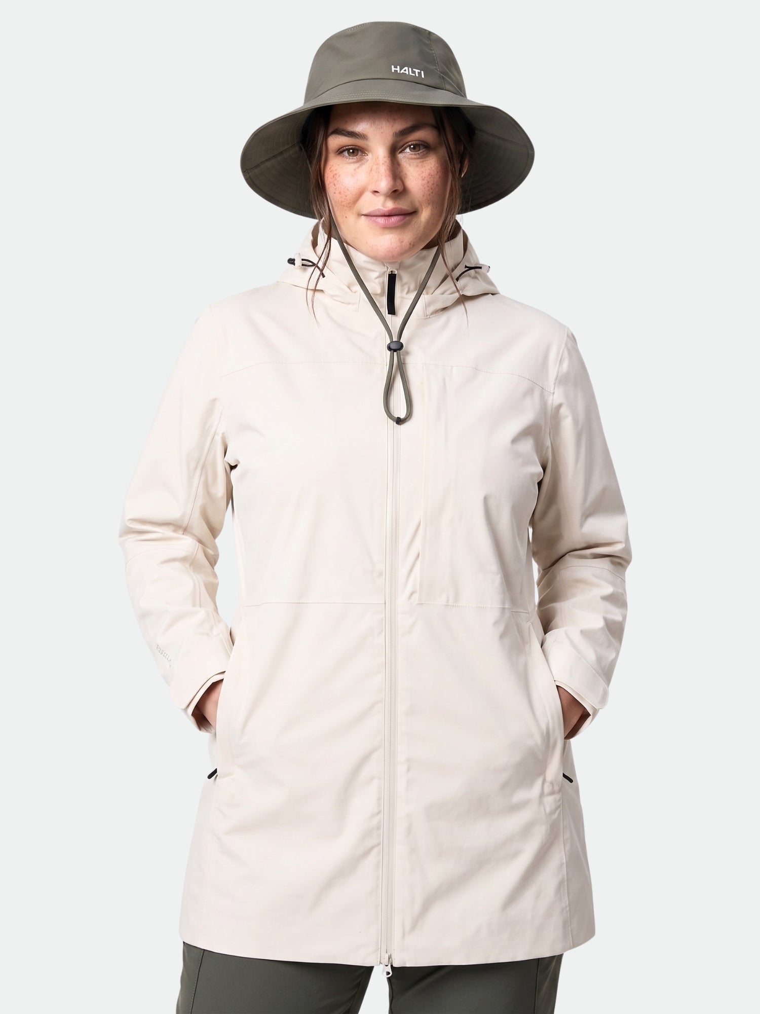 Eine Frau trägt die Halti Kallas DX Parka Jacke Plus für Damen und einen olivgrünen Hut mit breiter Krempe, die Hände in den Taschen.