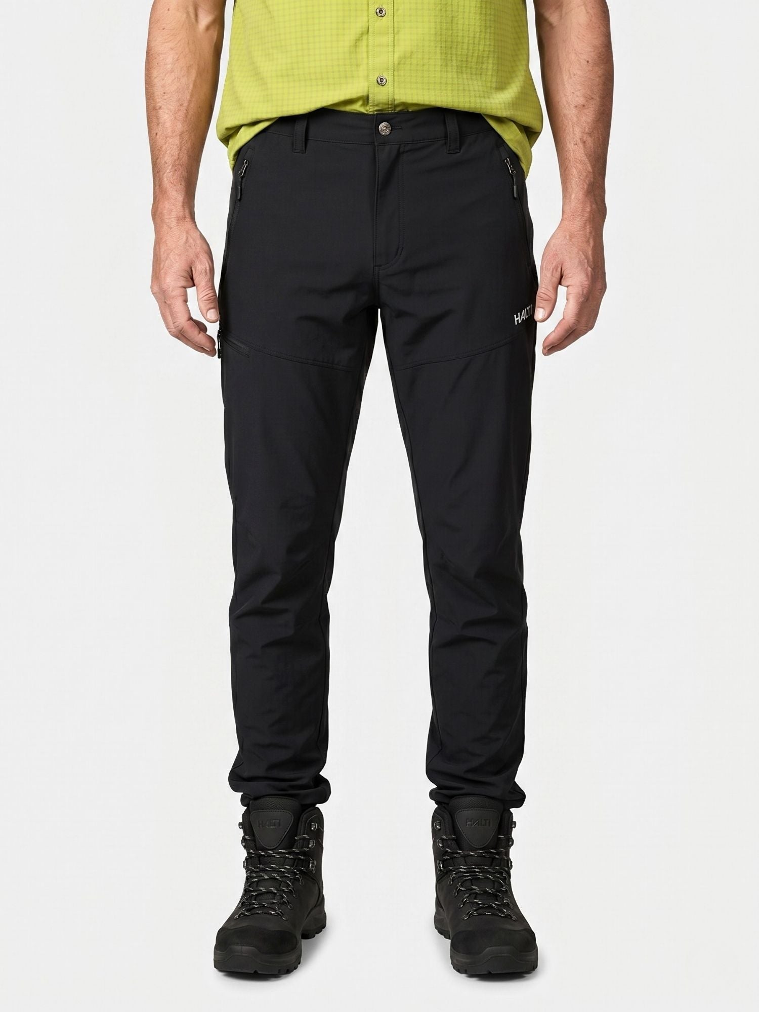 Eine Person in einem grünen Hemd und Halti Pallas Cool X-stretch Hosen Herren steht vor einem unifarbenen Hintergrund.