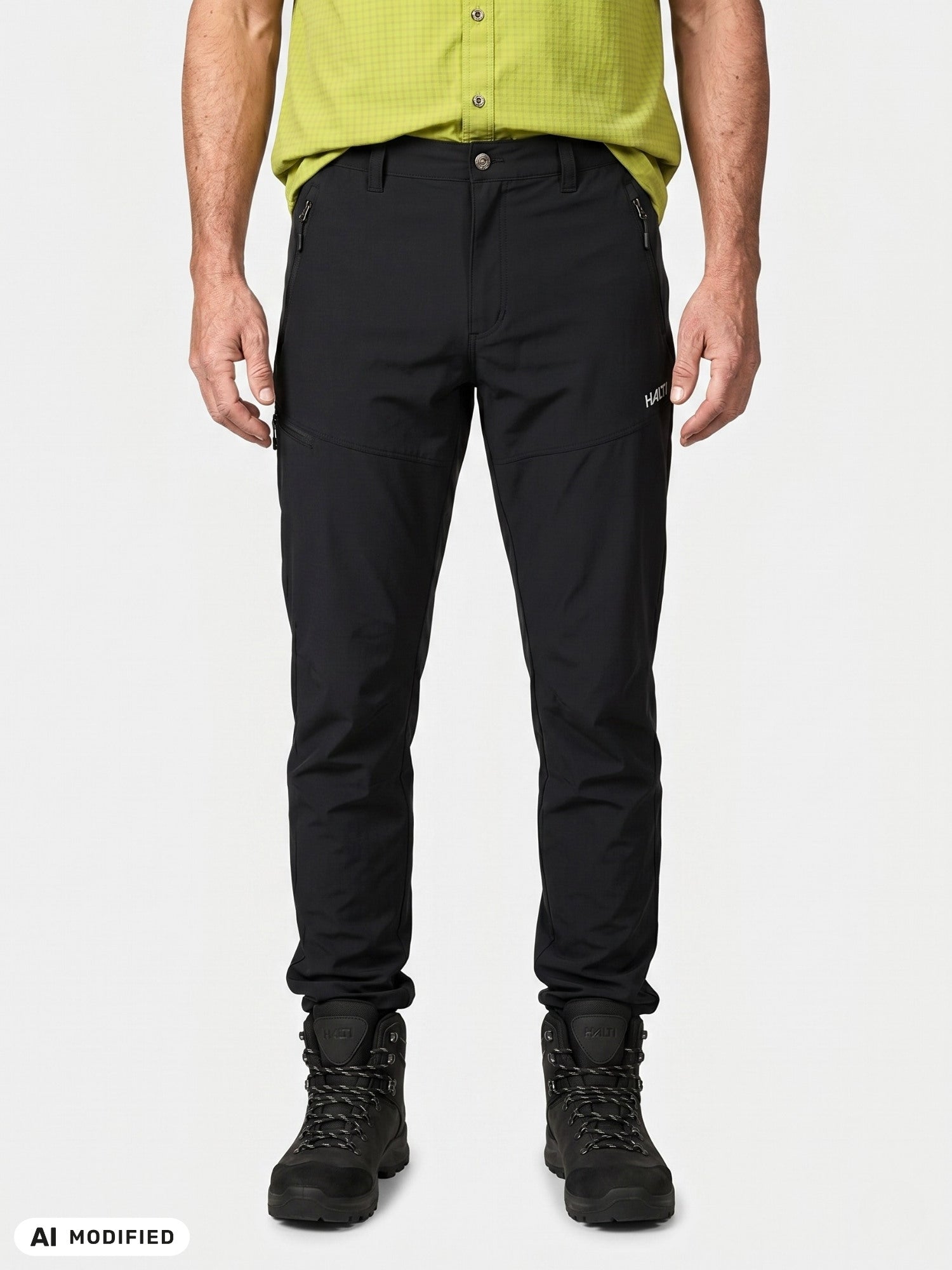 Ein Mann, der eine Halti Pallas Cool X-Stretch-Hose und Wanderstiefel trägt sowie ein hellgrünes Hemd, blickt vor einem einfarbigen Hintergrund nach vorne.