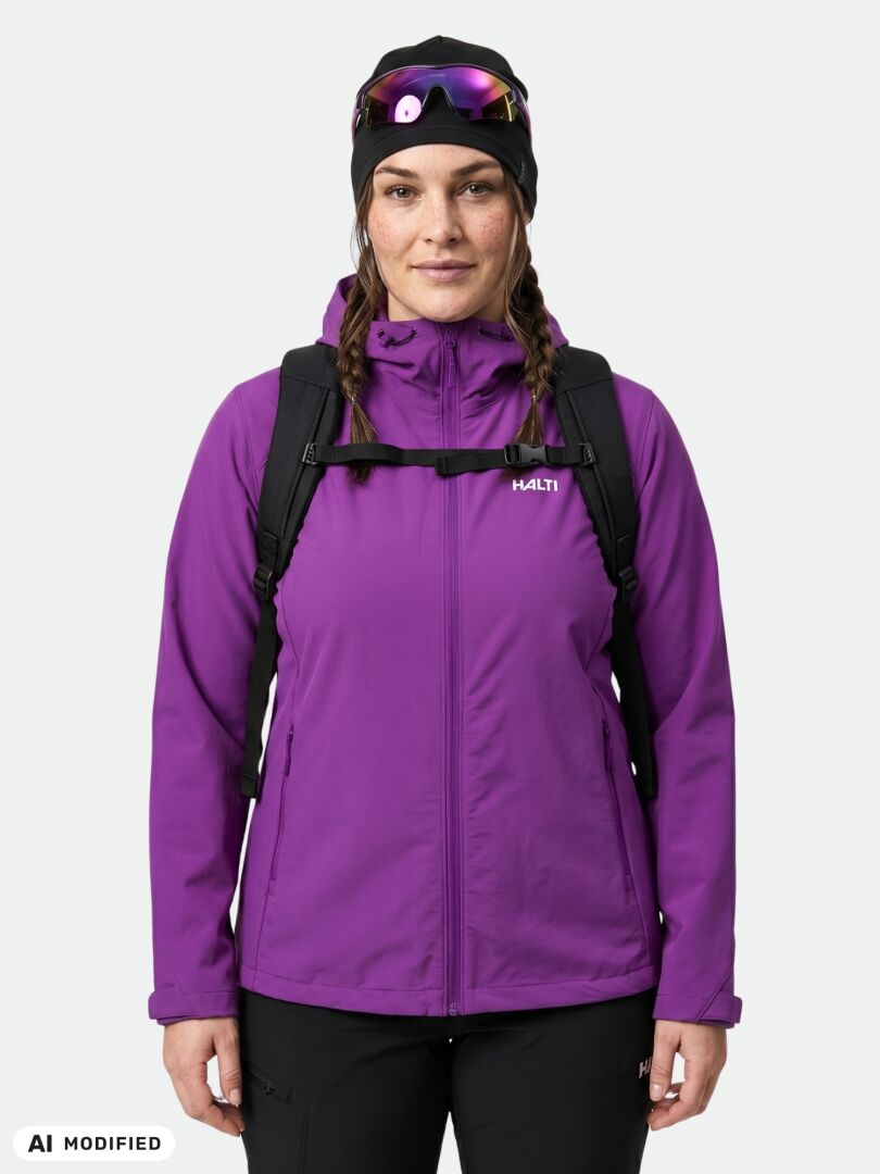 Eine Frau in einer violetten Halti Finholma X-Stretch-Jacke für Damen in Übergröße, mit schwarzem Rucksack, Mütze und Sonnenbrille tritt nach vorne.
