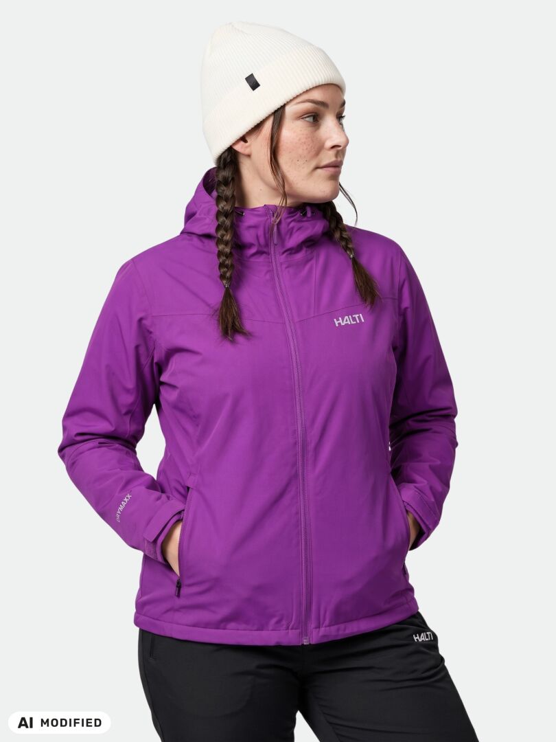 Eine Frau in einer violetten Halti Finholma X-Stretch-Jacke für Damen in Übergröße steht da, die Hände in den Taschen, und schaut zur Seite.