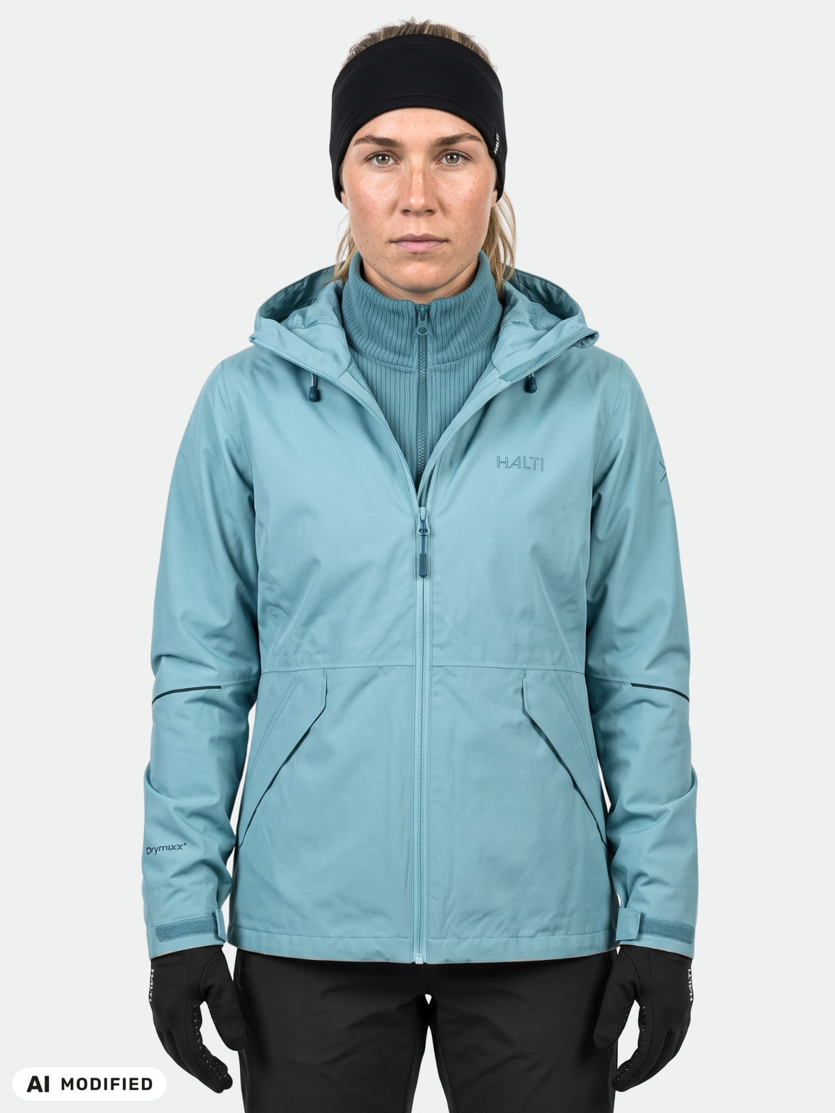 Eine Person in einer hellblauen Halti Loito 3in1 DX-Jacke für Damen, schwarzen Handschuhen und einem Stirnband blickt direkt in die Kamera.