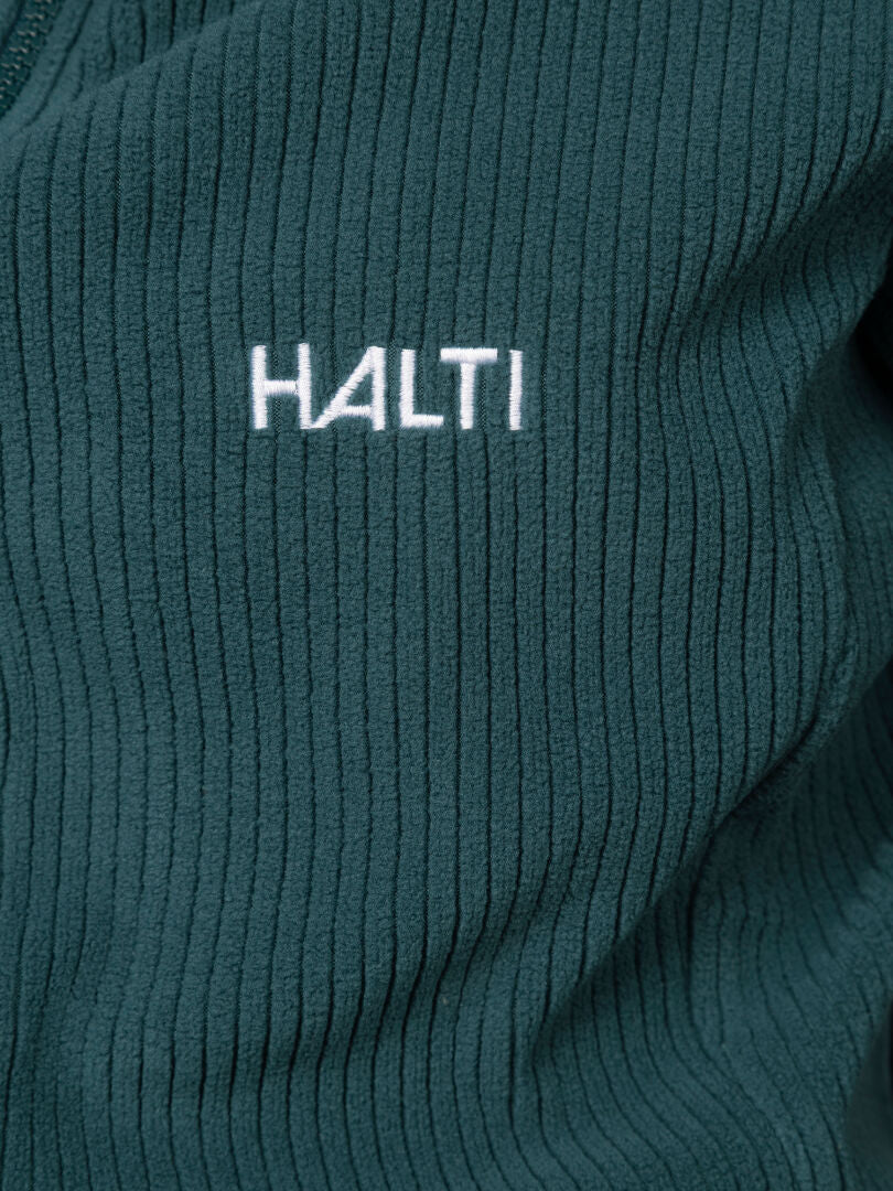 Nahaufnahme des dunkelgrünen, gerippten Stoffes der „Loito 3-in-1 DX Jacke Damen“ mit der weißen Stickerei „Halti“.