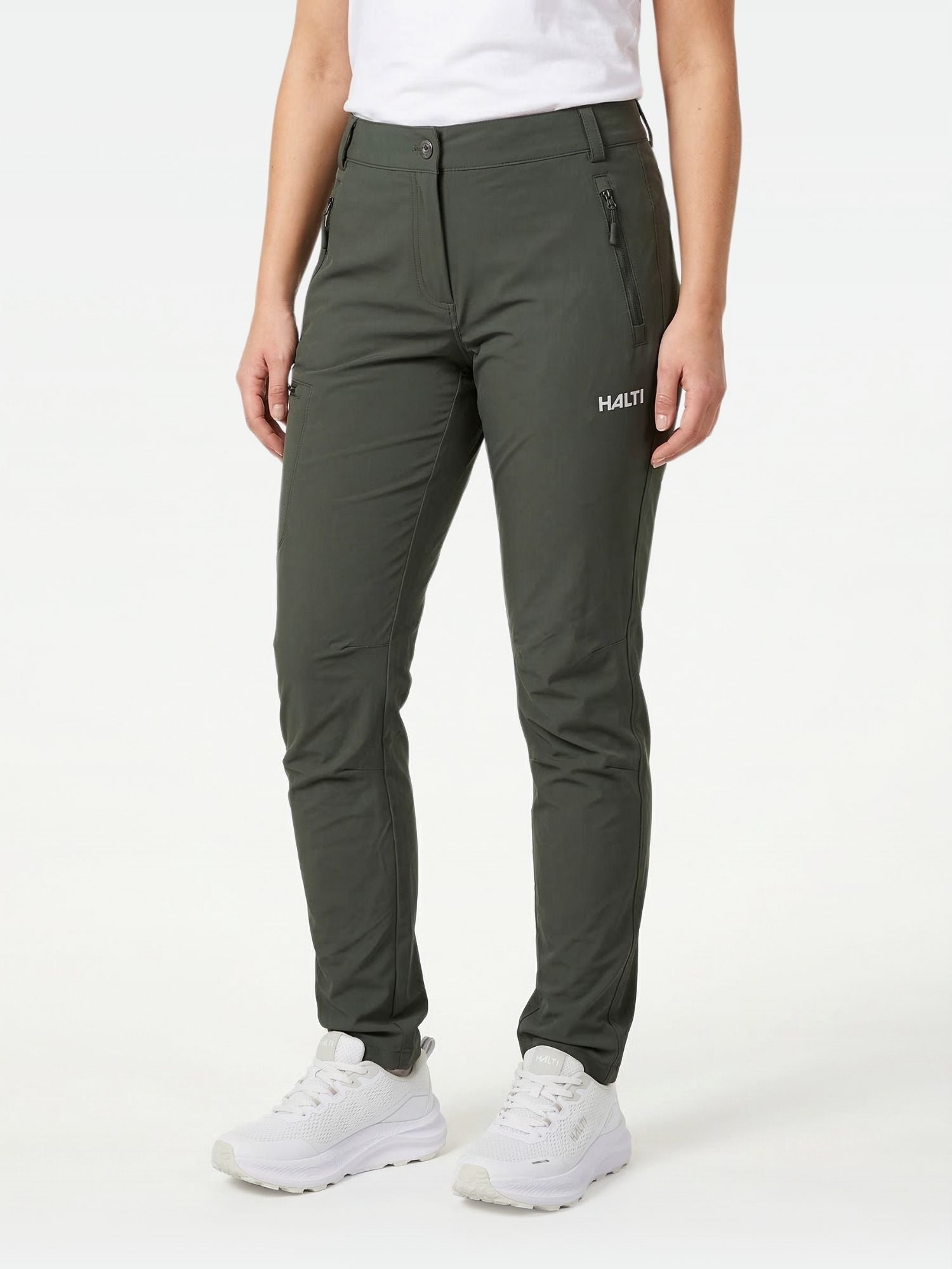 Person trägt dunkelgrüne Halti Pallas X-stretch Hose Damen mit Zipper-Taschen, weißem Shirt und weißen Schuhen.