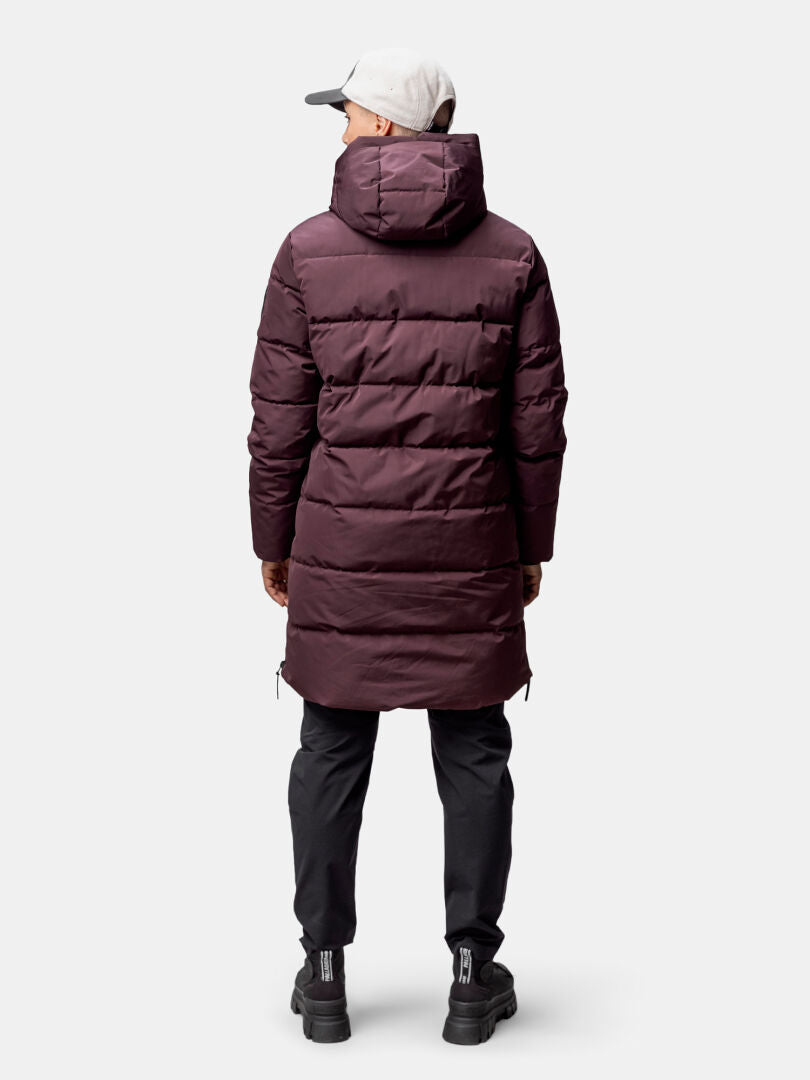 Person, die eine kastanienbraune Halti Linjat Parkajacke Damen, eine schwarze Hose, schwarze Schuhe und eine hellgraue Mütze trägt, von hinten gesehen.