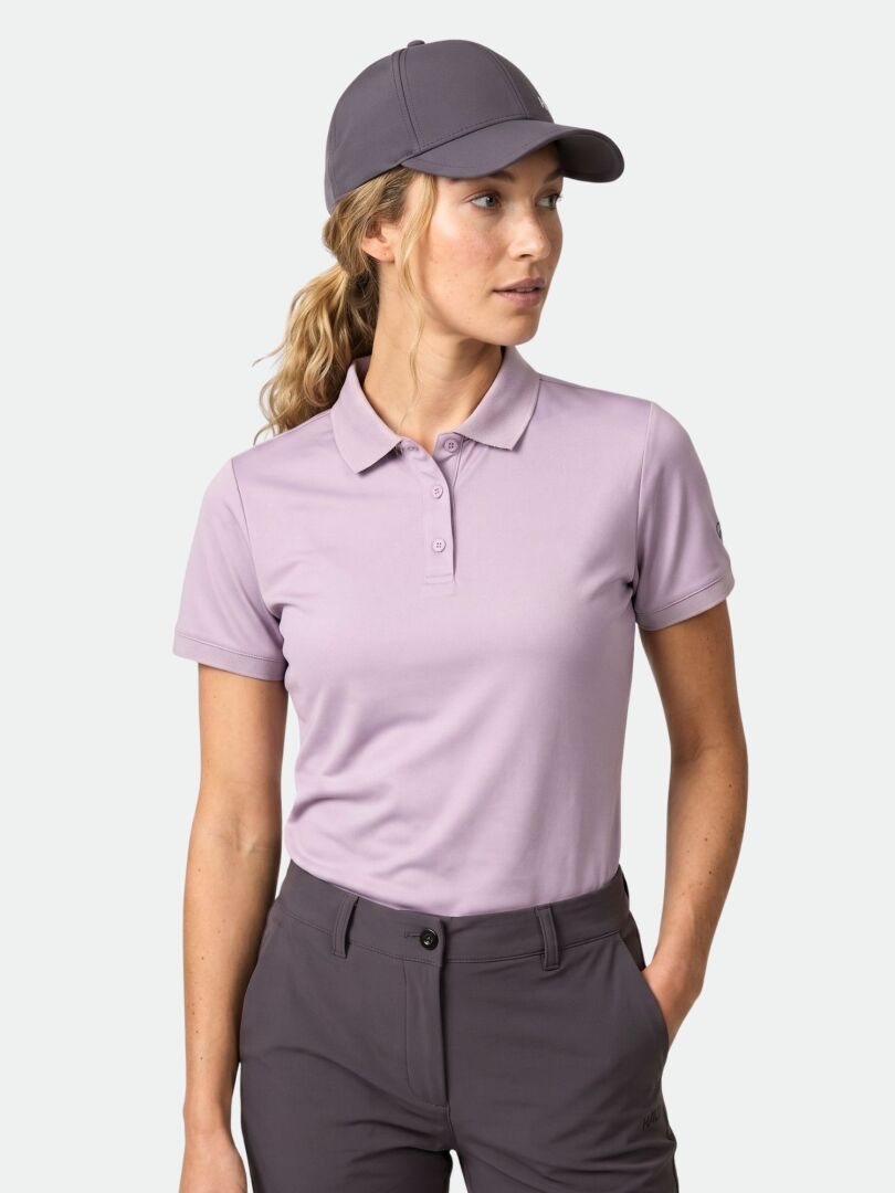 Frau trägt das Halti Laine Technisches Poloshirt Damen in hellviolett, dunkle Hosen und eine graue Mütze, Hand in der Tasche.