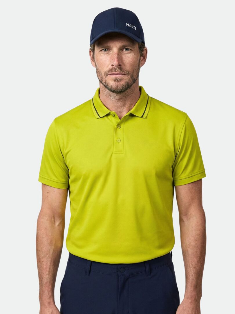 Mann in Halti Laine Technisches Poloshirt Herren, marineblauer Hose und Mütze steht vor einem schlichten hellen Hintergrund.