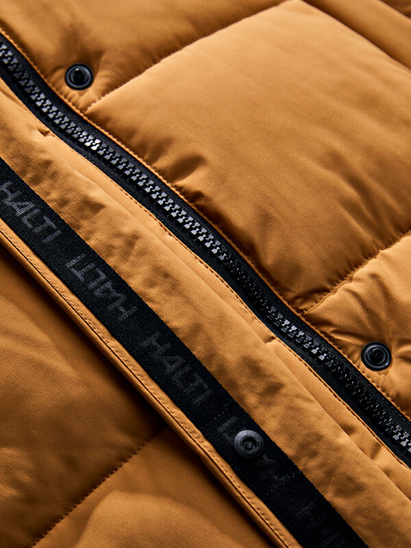 Nahaufnahme der „Halti Brahe Puffer Long Winterjacke Damen“ mit Reißverschluss, schwarzen Druckknöpfen und Logo-Band-Detail.