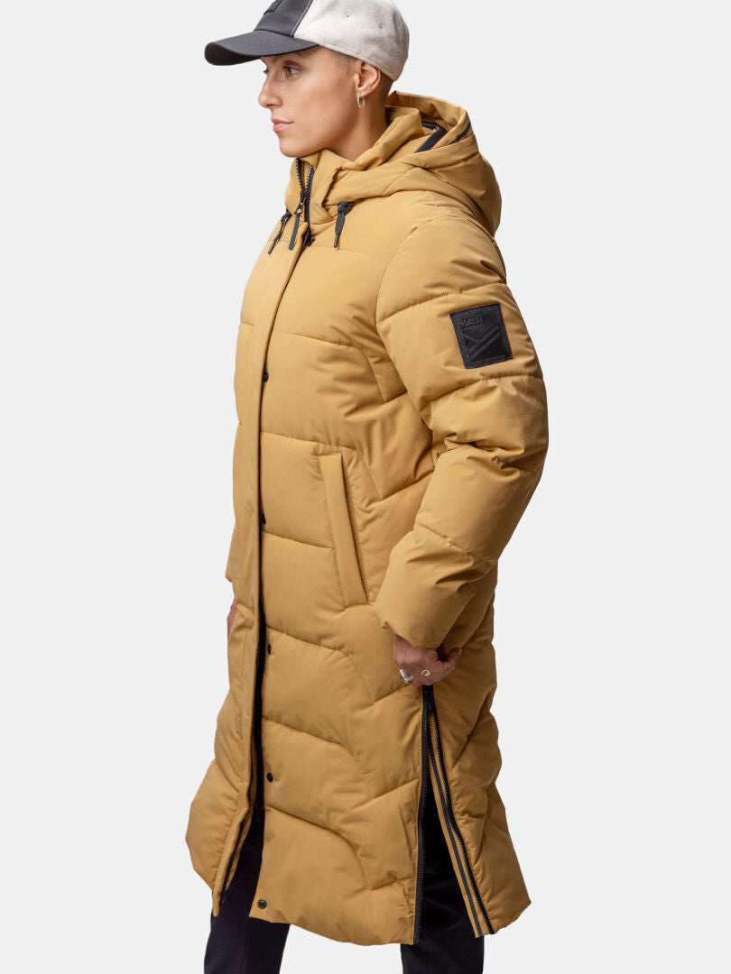 Person trägt Halti Brahe Puffer Long Winterjacke Damen mit Kapuze, seitlichen Reißverschlüssen und einer Baseballmütze.