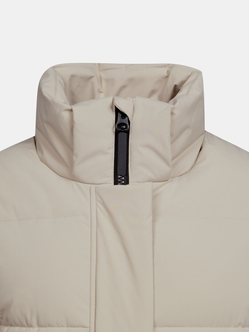 Nahaufnahme der „Halti Brahe Puffer Long Winterjacke für Damen“, beige, mit hohem Kragen und teilweise geöffnetem schwarzem Reißverschluss.