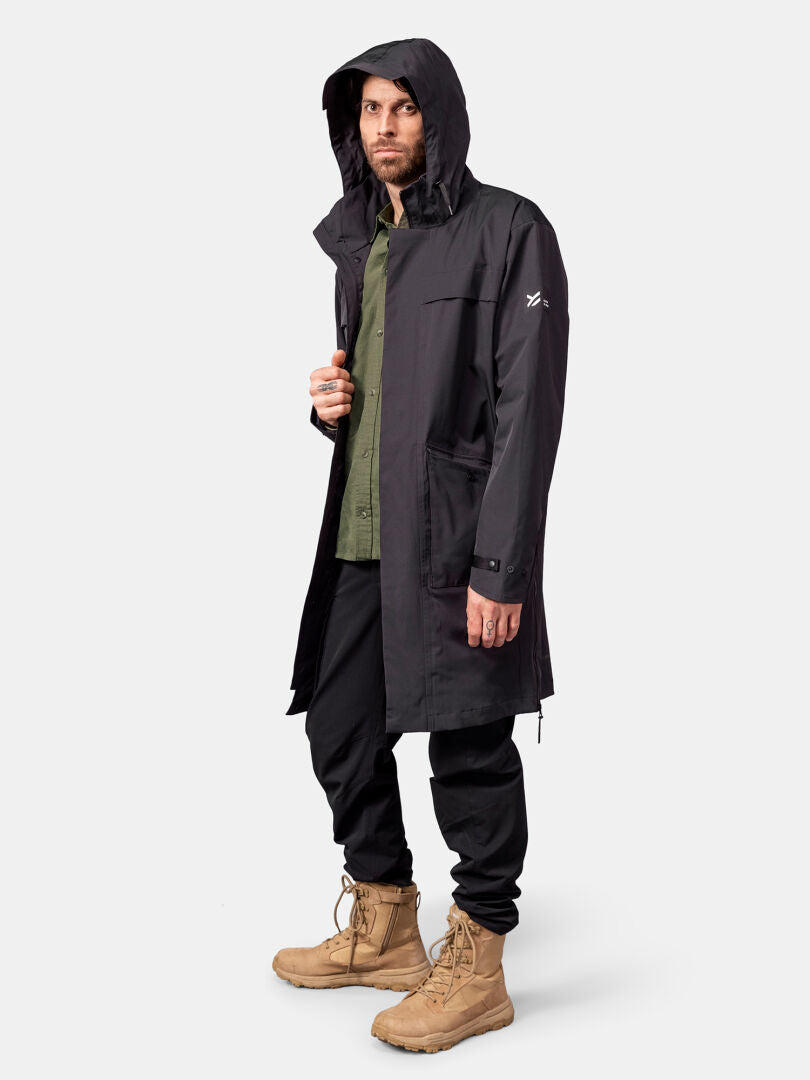 Ein Mann trägt die Halti Tokoi II DX Parka-Jacke für Herren in Schwarz, ein grünes Hemd, eine schwarze Hose und hellbraune Stiefel.