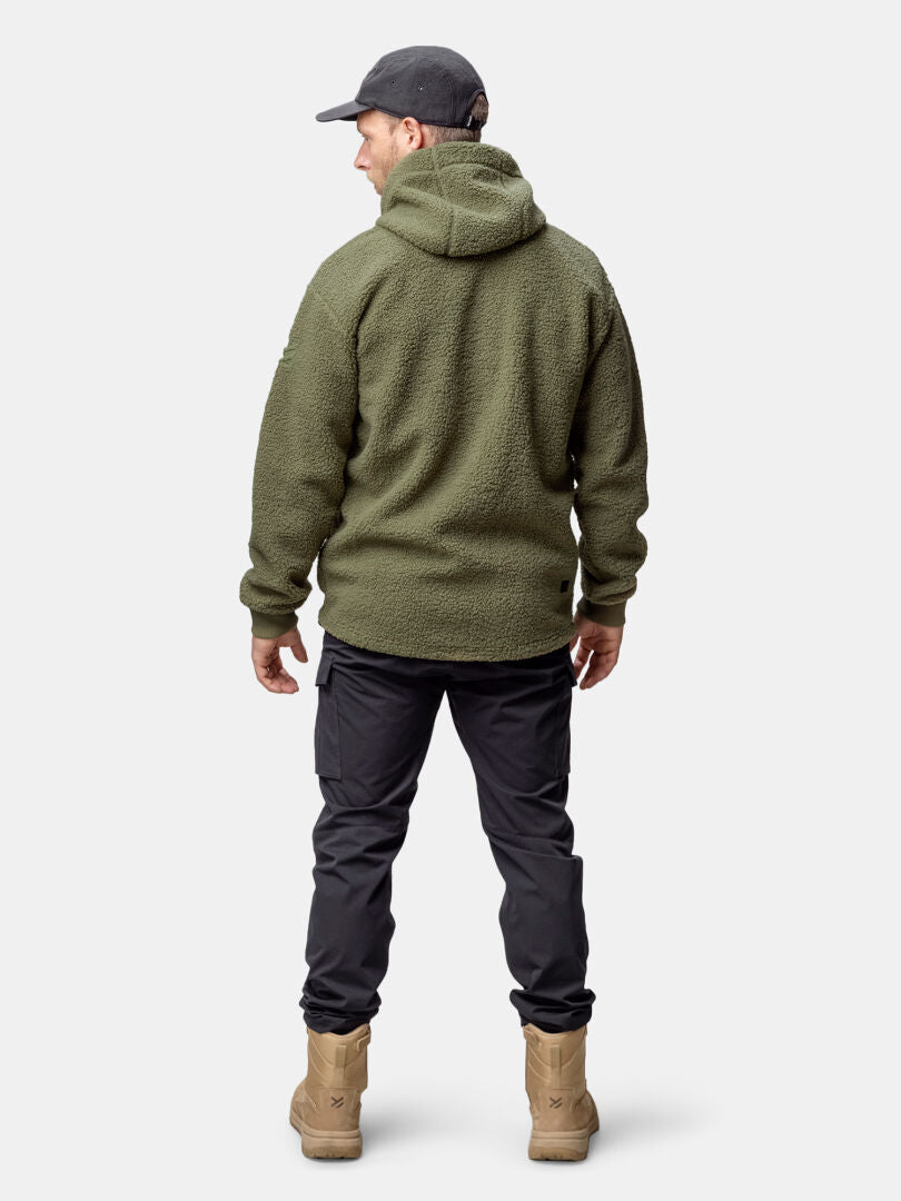 Ein Mann trägt eine Halti Lykky Fleece Jacke Herren, schwarze Hose und Tan-Boots, steht mit dem Rücken zur Kamera.