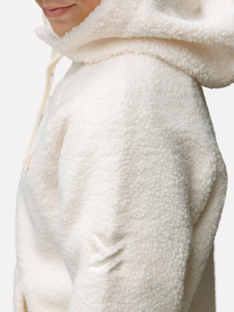 Frau trägt einen cremefarbenen Halti Lykky Fleecepullover Damen mit dezentem Ärmellogo, der leicht zur Seite zeigt.