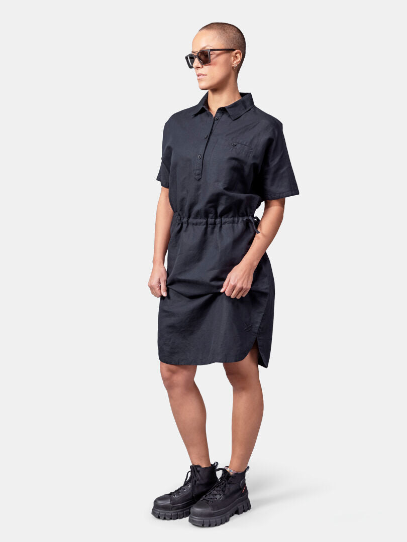 Person mit Sonnenbrille, einem Halti Notsgi Kleid Damen und schwarzen Stiefeln vor einem weißen Hintergrund.