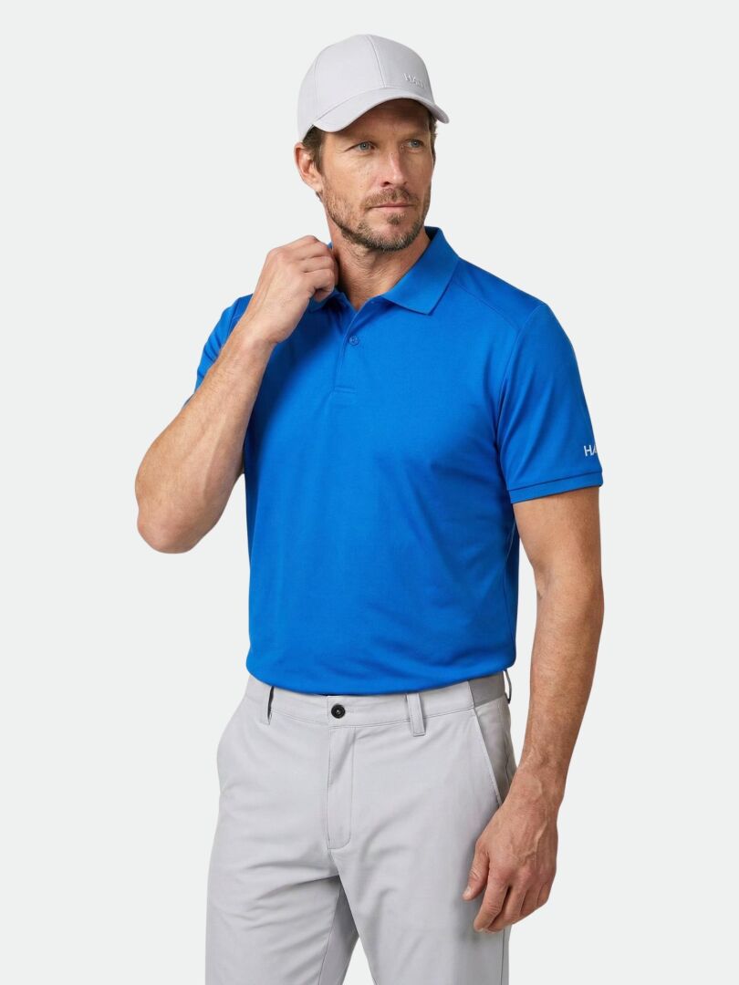 Mann trägt ein Halti Aridi Technisches Poloshirt Herren in Blau, eine hellgraue Hose und eine weiße Mütze vor einem weißen Hintergrund.